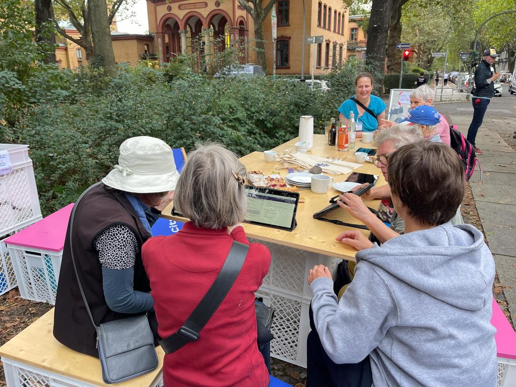 Mehrere ältere Personen sitzen an einem Tisch vor dem Kiezlabor und bedienen Tablets