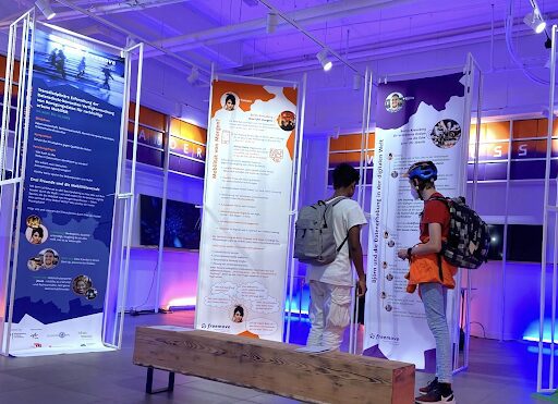 There are two boys, one wearing a helmet, taking a closer look at an exhibition on mobility data.
