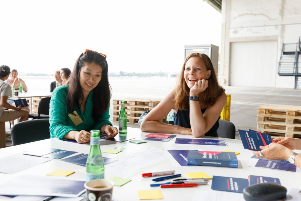 Two people sitting a table. Pen and papers are spreaded for a workshop.