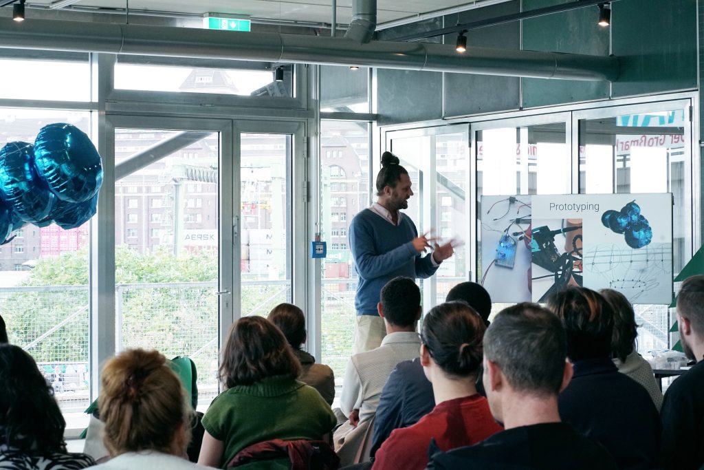 Ein Student erklärt beim Workshop der Summer School 2025 im CityLAB Berlin das Thema Prototyping vor einer Gruppe von Teilnehmenden und Gästen.