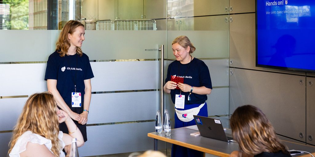Workshopleiterinnen Anna Meide und Anna Eschenbacher tragen vor einer Gruppe von Workshop-Teilnehmenden bei der CityLAB Sommerkonferenz 2025 vor.